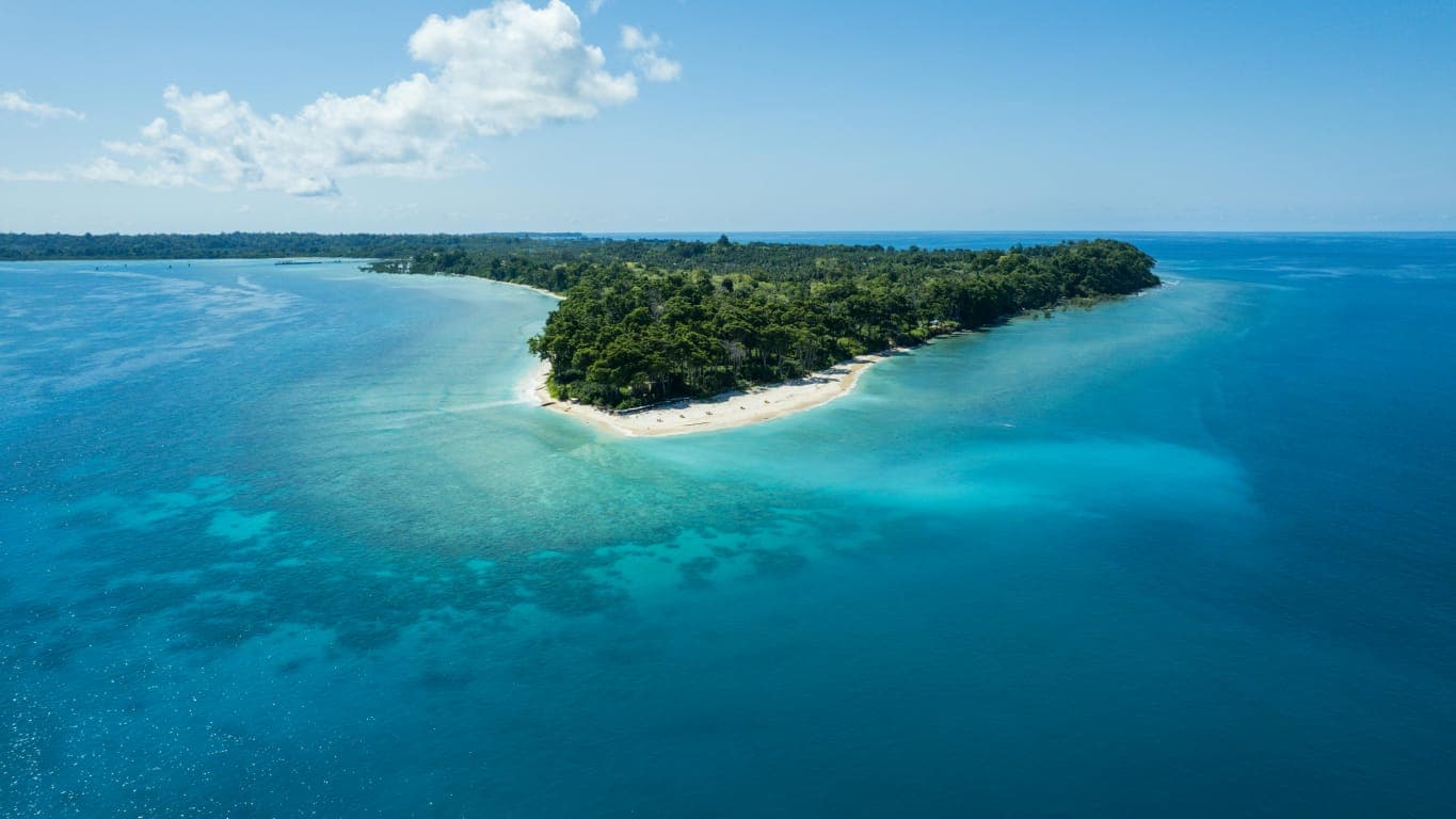 Aerial view of a forested Andaman island surrounded by turquoise and deep blue ocean
